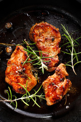 Fried pork tenderloin divided into portions with the addition of herbs and spices in the pan, close-up