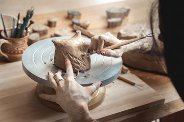 Craftsperson Concept. Young woman making pottery indoors making shape for clay using tool back view details close-up