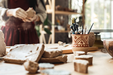 Craftsperson Concept. Young woman making pottery indoors tabl with creations material and tools close-up blurred background - obrazy, fototapety, plakaty