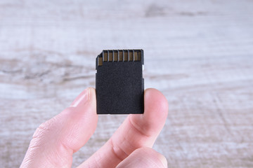 Hand holds flash drive, memory card adapter on wooden background. close up