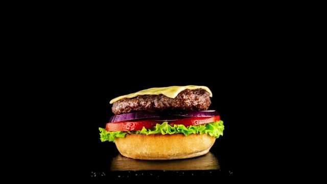  Beefsteak on a black background. Fresh tasty burger on a black background. Burger with beef, cheese, bacon and vegetables. Classic burger. Burger styling Big tasty hamburger with popping ingredients