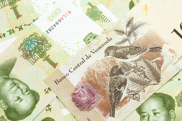A Venezuelan one hundred Bolivares bank note, close up in macro on a bed of Chinese one yuan bank notes