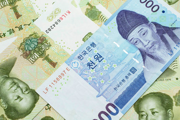 A blue South Korean one thousand won bank note close up in macro on a background of Chinese one yuan bank notes