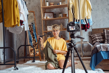Young adult vlogger sitting at home, showing her clothes on camera