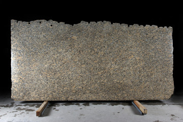 A large slab of natural yellow stone with dark dots called granite Phoenix Yellow