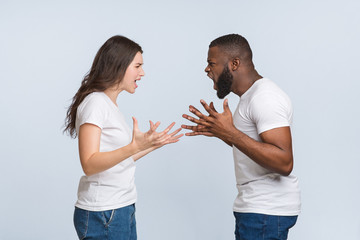 Angry interracial couple quarrelling, yelling at each other and emotionally gesturing