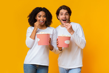 Young multiracial couple eating popcorn from buckets and looking at camera