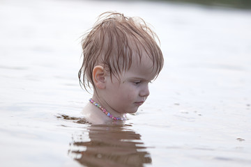 Fototapeta premium little independent girl sitting in the water on the lake