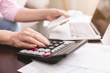 Senior woman calculating taxes at home, using calculator