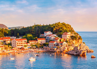 Fototapeta premium Picturesque summer view of Adriatic sea coast in Budva Riviera. Przno village with buildings on the rock at sunset warm sunlight, Montenegro