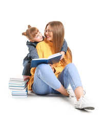 Beautiful young woman and her little daughter reading books on white background