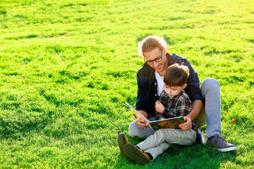 Naklejka na ściany i meble Father and his little son reading book outdoors