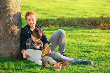 Father and his little son reading book outdoors