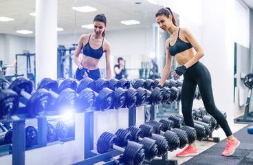 Fototapeta na wymiar Young and beautiful woman working out with dumbbells in gym. Healthy life and sport fit