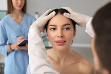 Plastic surgeon examining young woman's face prior to operation in clinic