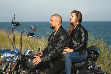 biker couple in leather clothes against the cool expensive bike. hot woman in leather jacket bra and jeans and brutal man smoking and riding motorcycle