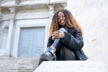 A happy black afro girl with curly brown hair sitting and looking at the camera on a cloudy day