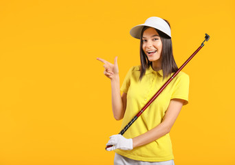 Beautiful female golfer pointing at something on color background