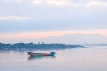 Landscape  of green boat floating on the Mekong in the morning. The sky behind is cloudy and very foggy but cat see shadow of the mountains.