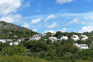 Fototapeta na wymiar Cloudy rocky mountain with grass, trees and houses. Ibiza island, Spain
