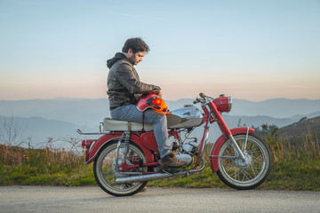 motard homem sentado na moto vermelha antiga ao pôr do sol nas montanhas