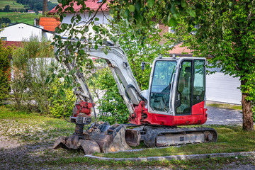 Small stopped excavator with a shovel parked under a tree
