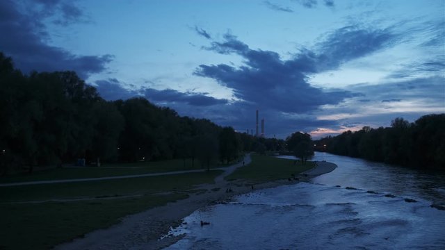Munich nature at dramatic dusk: autumn in park of tourist Bavarian city. View of Isar river, trees and St Maximilian church from Reichenbach Bridge. Munchen, Bavaria, Germany. Camera horizontal pan