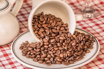 Roasted coffee beans in cup and plate on coffeeshop table. Fresh gourmet flavor aroma. Delicious fair trade cafe cappuccino or espresso ingredient. The bean bunch was fallen over at breakfast