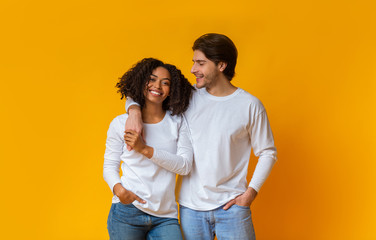 Happy multiracial couple hugging and posing together over yellow background