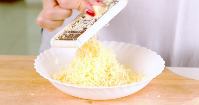 Closeup of woman hand grating cheese with a grater in the kitchen at home