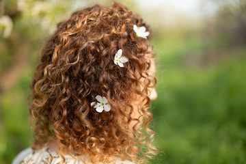 Attractive young woman with white flowers woven in her curly hair. Spring fashion concept