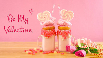On-trend Valentine's Day table setting with pink strawberry freak shakes topped with heart shaped lollipops, donuts and cotton candy, with Be My Valentine text greeting.