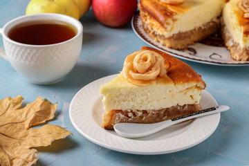 Cheesecake with apples located on a light blue background, decorated with roses from apples and cup of tea, Closeup
