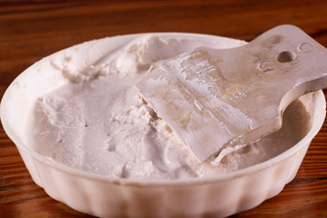 Close-up plastic container with putty and rubber spatula.
