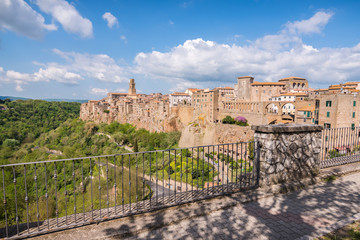 Panoramic view of Pitigliano small vilage in Italy with red brick houses and towers and nature at golden hour with beautiful sky clouds and fence in Grosseto province in Tuscany Italy