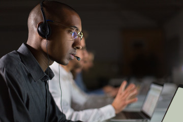 Focused call center operator communicating with client. African American young man in eyeglasses...