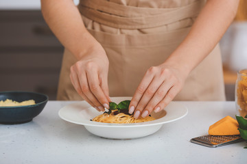 Woman preparing tasty pasta with tomato sauce on table in kitchen, closeup