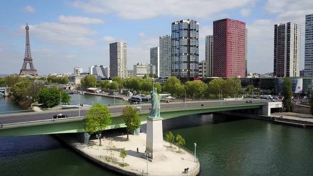 A reverse aerial recording of the statue of liberty in Paris. The Eiffel Tower and a couple of skyscraper are visible in the background.