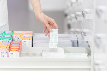 Pharmacist holding medicine box and capsule pack in pharmacy drugstore.