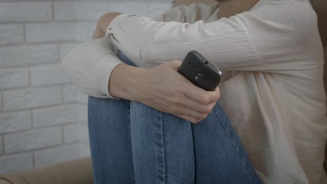 Depression with a smartphone. A woman sits in a closed position and holds a smartphone in her hands.