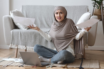 Concerned muslim girl freelancer with papers and laptop at home