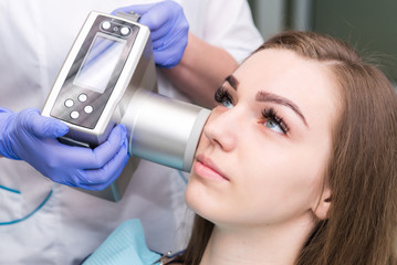 Dentist prepares to make tooth x-ray image for young girl in dental clinic.