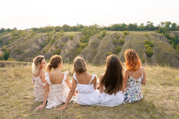 Shoot from back. The company of female friends having fun and enjoy hills landscape.