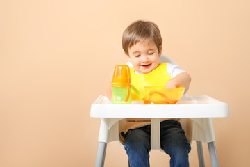 Cute little boy eating tasty baby food against color background