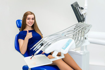 Young girl patient smiles and shows thumb up in the doctor’s chair in the dental office