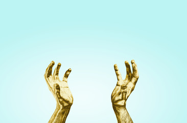 Golden hands raised up on a blue pastel background. The concept of preaching ideas, raising hands up to catch something. Golden-colored hands reach for the sky.
