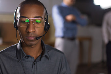 Focused African American man with headset looking down. Front view of call center operator. Call...