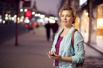 Woman using smartphone on the street in the evening. People, technology and lifestyle concept