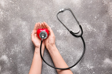 Female hands with heart and stethoscope on grey background. Cardiology concept