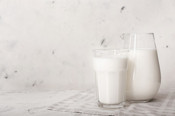 Glass and jug of tasty milk on white background